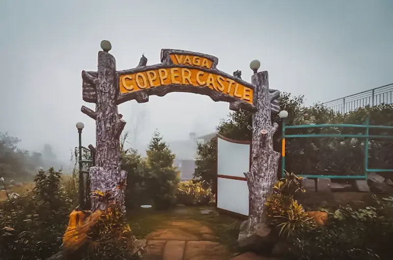 Decorative wooden entrance archway leading into Vaga Copper Castle resort premises in Vagamon