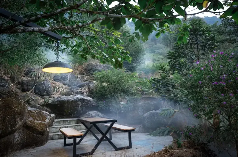 Wooden picnic table deck alongside natural rock waterfall stream at Ela Luxury Stay