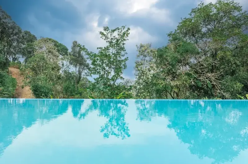 Outdoor swimming pool deck overlooking green mountain forest at Ela Luxury Stay Vagamon