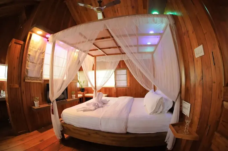 Rustic wooden treehouse bedroom interior with comfortable double bed and draped canopy at Orma Farm Resorts Vagamon
