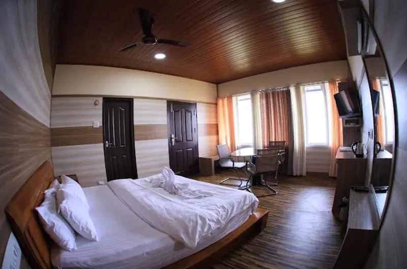 Spacious resort bedroom suite with plush double beds and warm wooden paneled walls at Orma Farm Resorts Vagamon