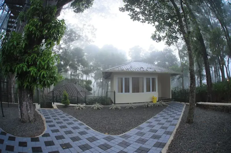 Wooden cottage exterior with paved stone walkway surrounded by trees at Orma Farm Resorts Vagamon