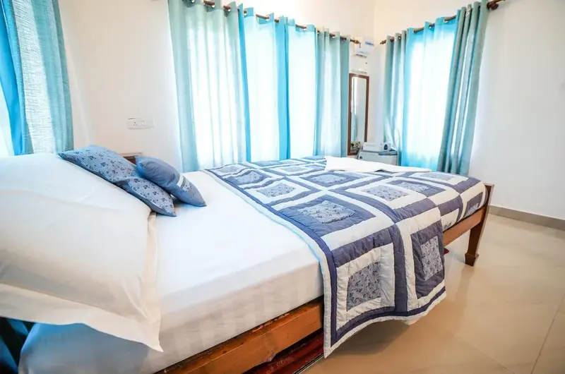 Brightly lit homestay bedroom featuring plush double bed and blue drapes at The Nest Homestay Vagamon