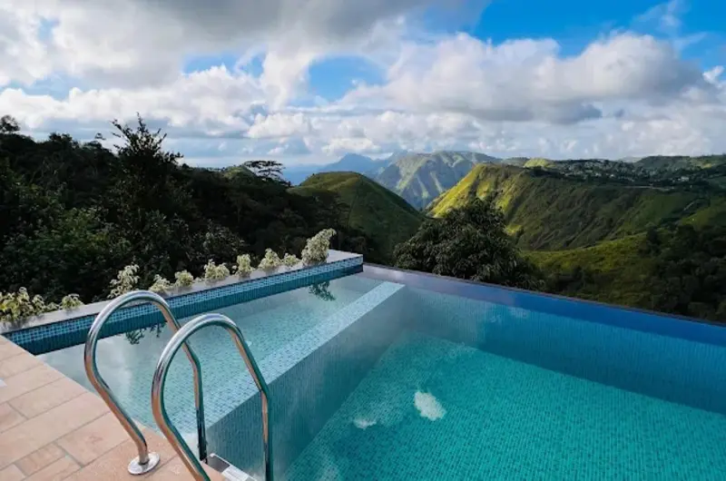 Infinity swimming pool with blue water overlooking scenic green hills at Trip Mount Vagamon