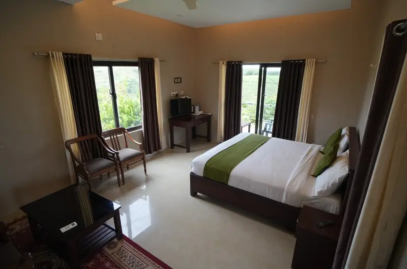 Deluxe guest room interior featuring double bed and seating near balcony at Cee Cee Grand Resort Vagamon