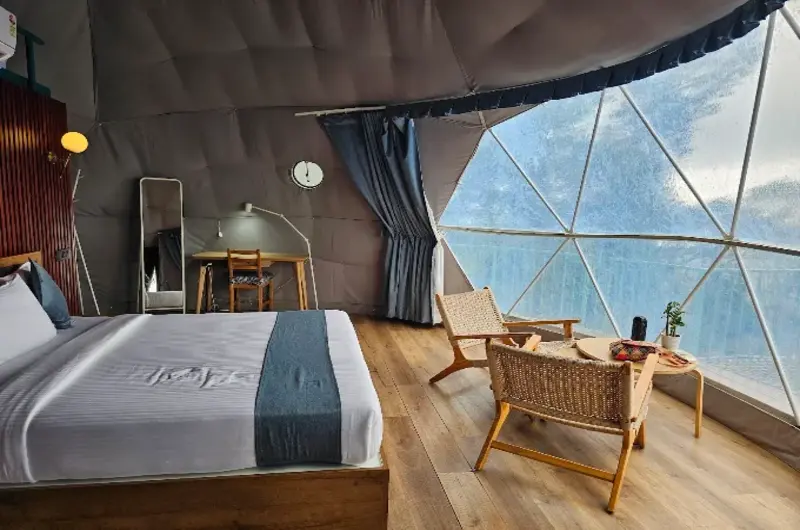 Interior bedroom setup featuring large panoramic window overlooking green hills at Willmount Geodesic Domes Vagamon