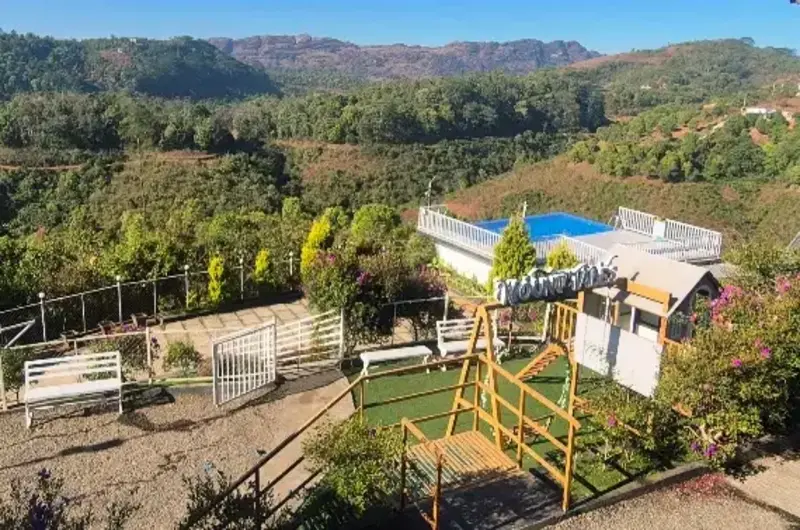Panoramic view of Nexstay Mount Tales resort buildings set against Vagamon mountains