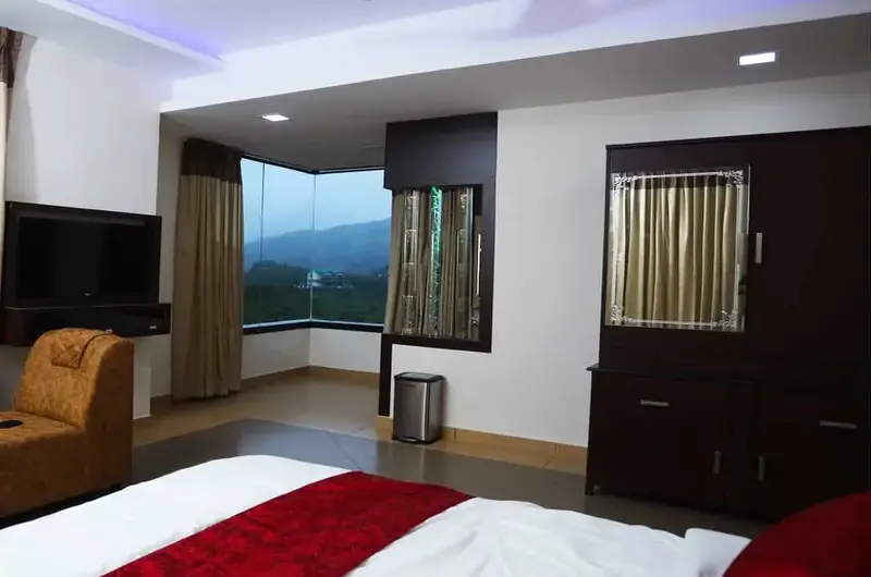 Deluxe guest room with large window overlooking green hills at Mountain Mist Resort Vagamon