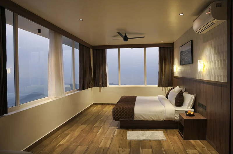 Deluxe resort bedroom featuring large scenic window overlooking Vagamon hills at Olga Resorts