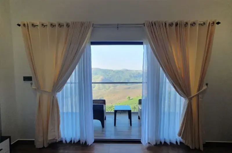 Balcony exit with glass doors and curtains opening to scenic hill views at The Felmel Resort