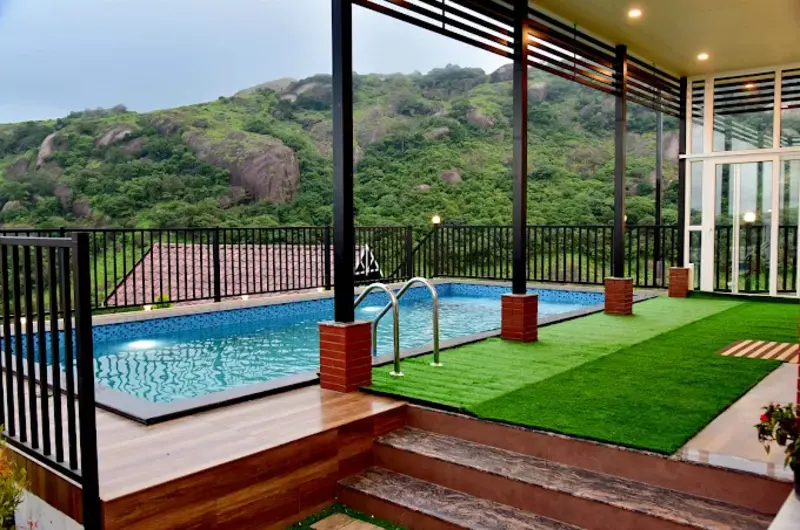 Outdoor swimming pool with sun deck overlooking lush green hills at ODMOR Resort Vagamon