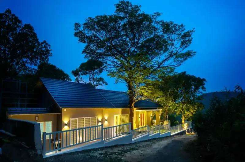 Exterior view of Willow House Cottages surrounded by trees under a deep twilight sky in Vagamon