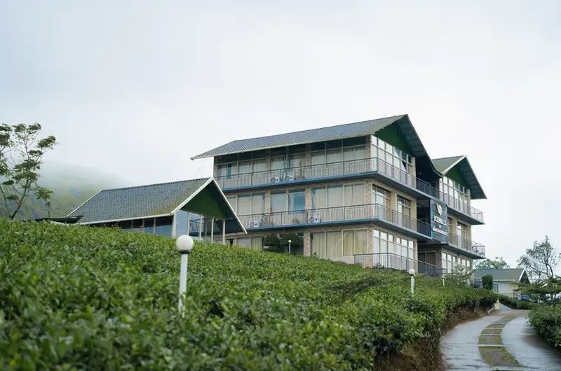 Modern multi-story building facade of Ice Hills Resort surrounded by green rolling hills in Vagamon