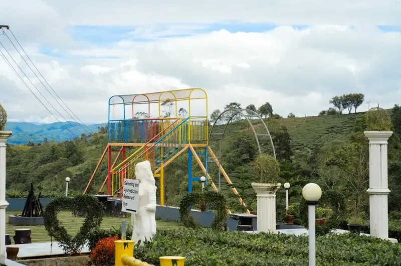Outdoor children play area and garden lawn at Ice Hills Resort with green hill backdrop