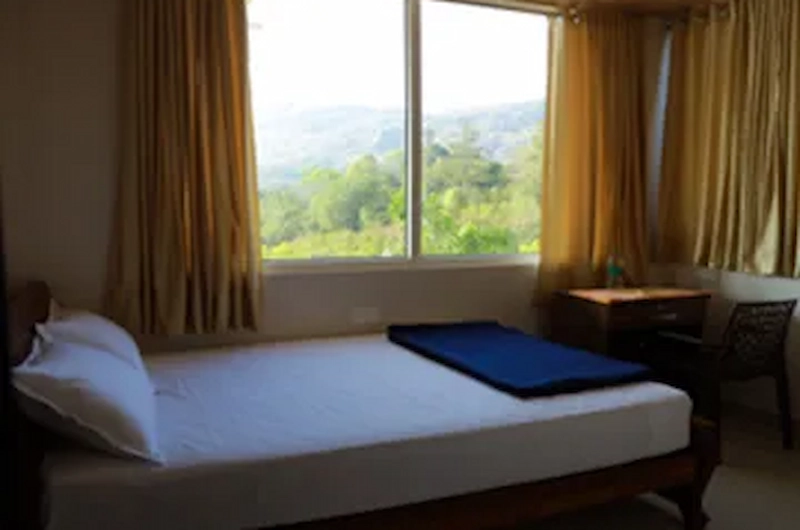 Cozy guest room bed next to a large window with scenic outdoor view at Vaga View Residency
