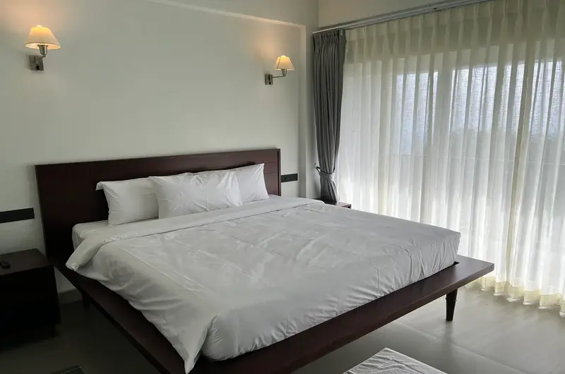 Spacious luxury bedroom suite featuring double bed, wall-mounted TV, and curtained windows at Vagamon Exotica