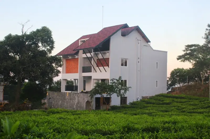 Side exterior view of white villa cottage surrounded by lush greenery at Vagamon Exotica