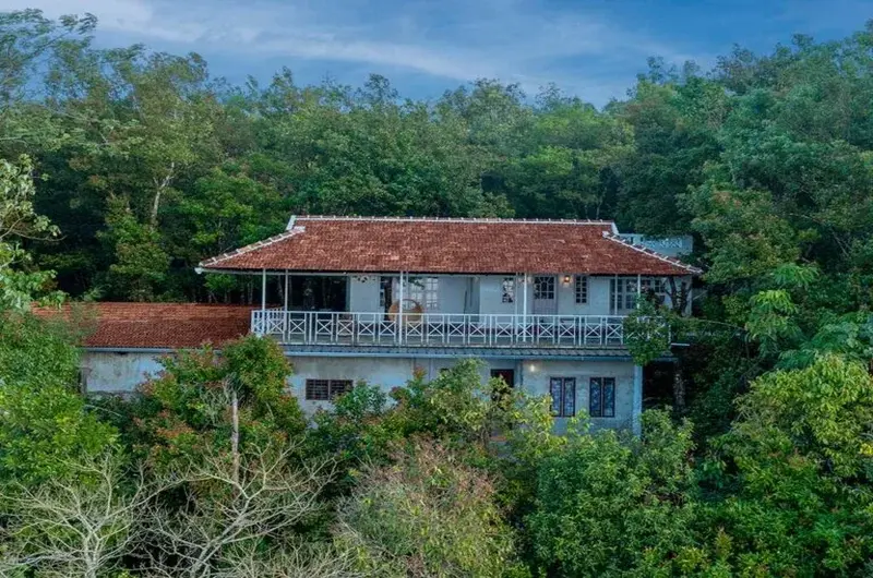 Exterior view of red-tiled roof cottage nestled among lush trees at Ghats Edge