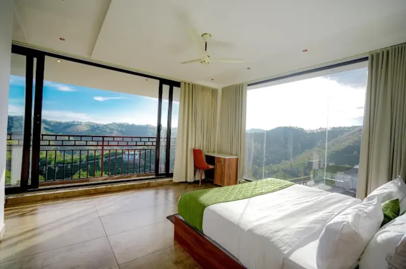 Resort bedroom with large panoramic glass window facing Vagamon hill views