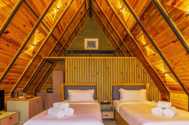 Cozy A-frame cottage interior featuring twin bed setup under slanted wooden ceiling in Vagamon
