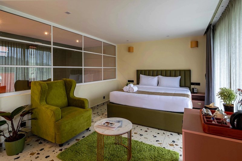 Modern guest room suite with green armchair, plush bedding, and floor-to-ceiling windows in Vagamon