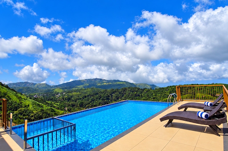 Infinity swimming pool with deck loungers overlooking misty green hills at Honeycomb Vagamon