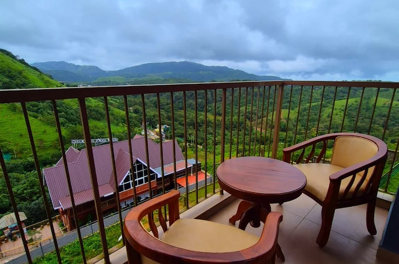Outdoor balcony seating area with wooden table and chairs overlooking green valleys