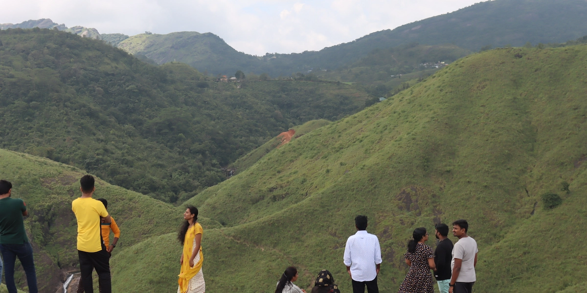 Tourists standing on green grassy hill slopes enjoying mountain landscape in Vagamon Kerala