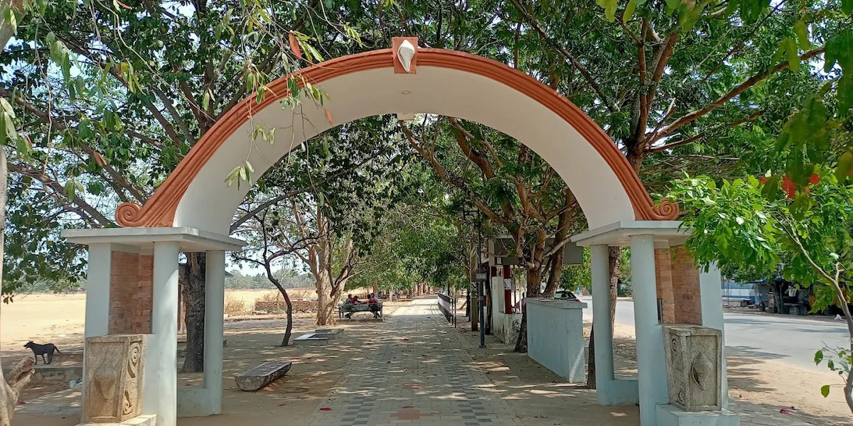 Arched stone gateway entrance at an ashram ground surrounded by trees and greenery in Kerala
