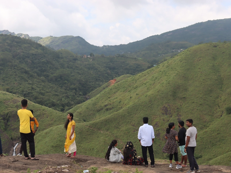 Group of visitors standing along hilltop ridge overlooking lush green valleys in Vagamon