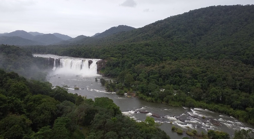 Scenic panoramic view of Athirappilly Waterfalls surrounded by lush green forests in Kerala